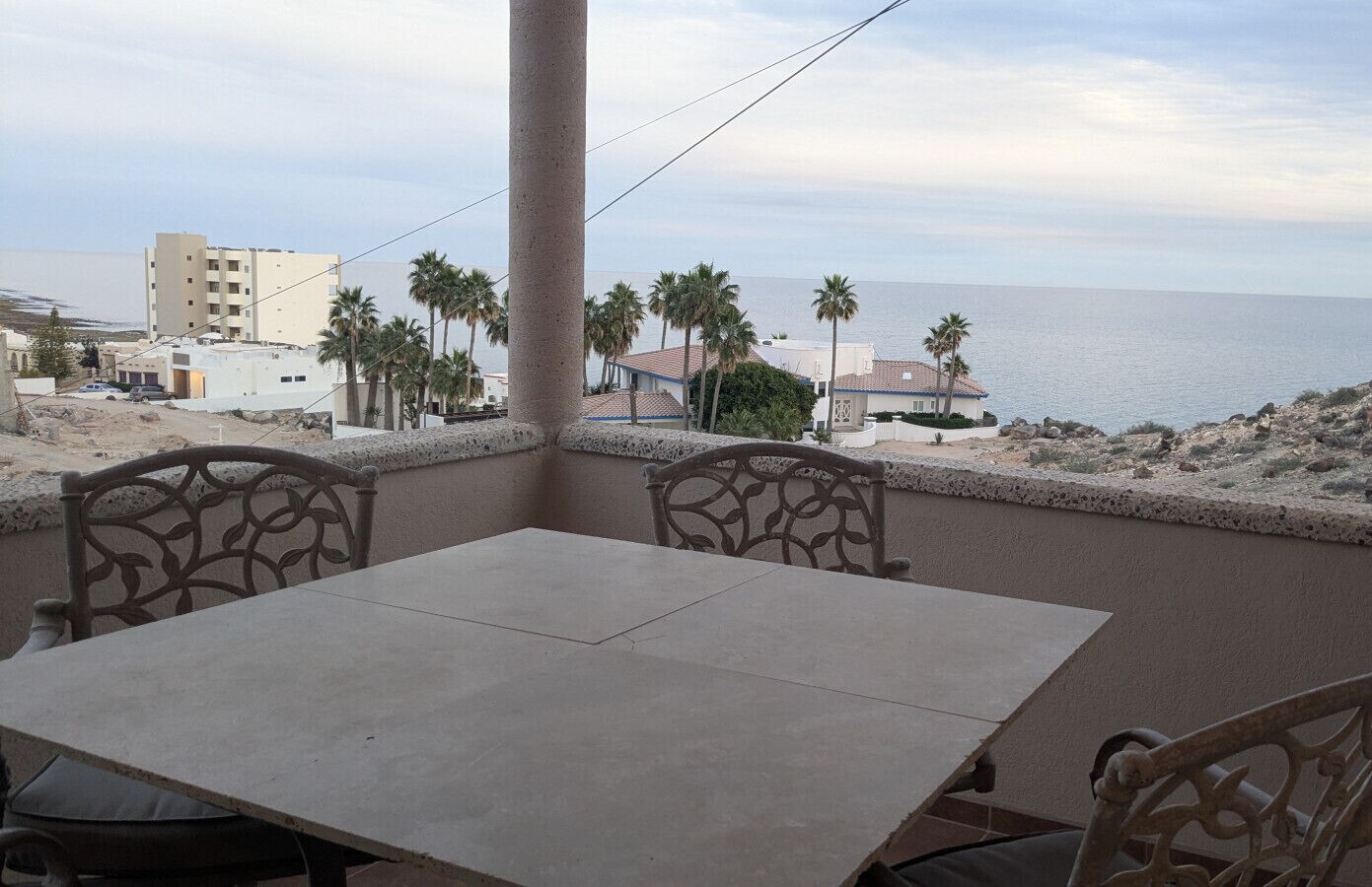 A balcony with a table and chairs, overlooking a beach and buildings.