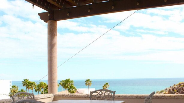 Una terraza con mesa y sillas con vista al mar, con palmeras y cielo despejado.