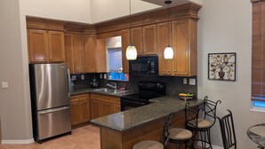 Una cocina con armarios de madera, electrodomésticos de acero inoxidable, encimeras de granito, luces colgantes y un elemento decorativo en la pared.