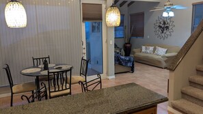Ein Essbereich mit einem runden Tisch und Stühlen, einer Küchenzeile, einer Treppe und einem Wohnzimmer mit einer Couch und Wanddekoration.