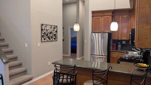 Una cocina con refrigerador de acero inoxidable, armarios de madera, encimera de granito y un comedor con sillas.