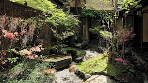 A traditional Japanese garden with a stone water feature, surrounded by various plants and trees. - Kyo no Yado Ishihara (Kyoto)