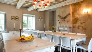 Un comedor con sillas blancas, una mesa de madera con un frutero y una lámpara de araña.