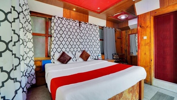 A hotel room with a bed, wooden walls, patterned curtains, and a red door.