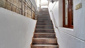 A narrow staircase with metal railings and a wooden handrail, leading to a door with a glass panel.