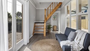 Un salon spacieux avec un escalier en bois, un canapé gris et une grande fenêtre.
