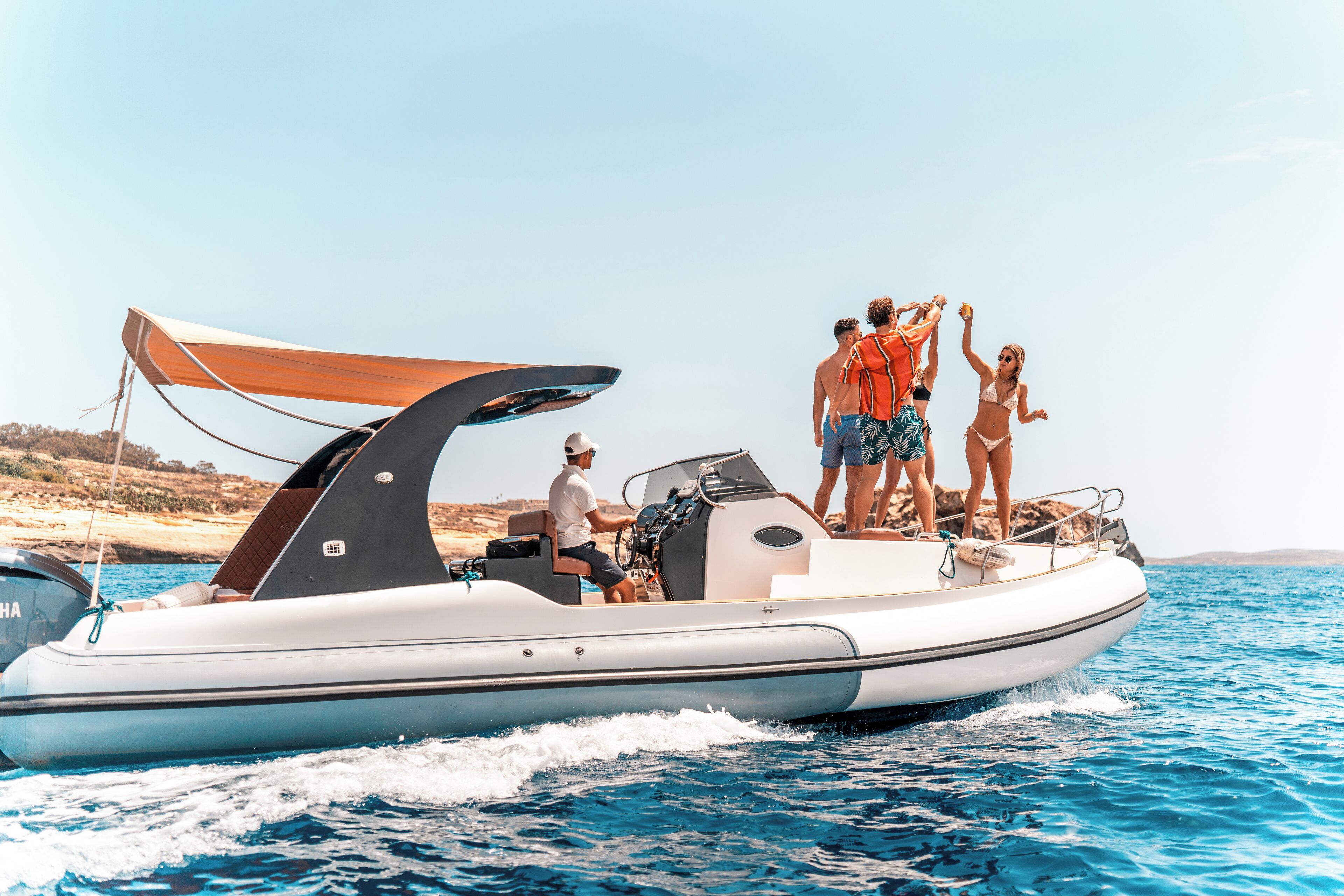 A motorboat with a canopy, passengers, and a rocky coastline in the background.