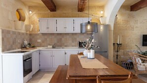 A kitchen with white cabinets, a wooden dining table, and a hanging light fixture. - Tal-Kitarra Villa (Kercem)
