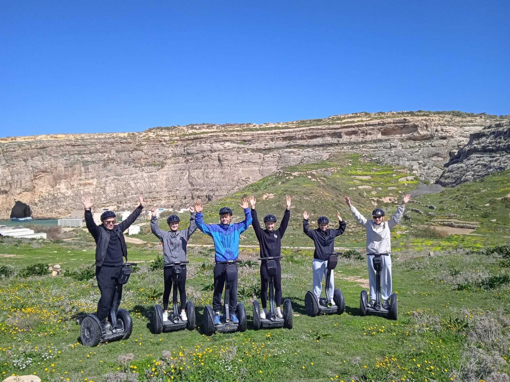 A group of people on segways in a grassy area with a rocky cliff in the background.