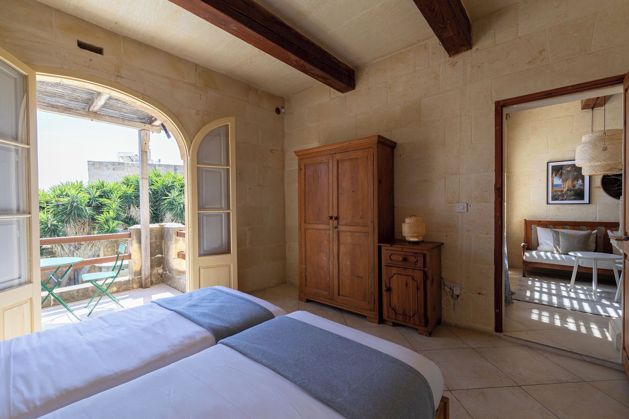Une chambre à coucher comprenant un lit, une armoire, une petite table avec une lampe et un balcon avec des chaises.
