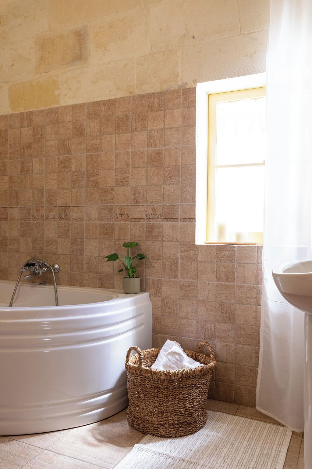 A bathroom with a bathtub, a sink, a potted plant, and a wicker basket.