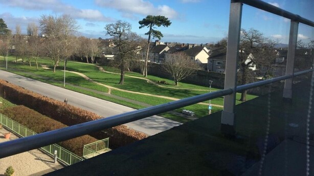 A view from a window overlooking a residential area with houses, a road, and a grassy park. - Central Spacious 3 Bedroom Apartment With Parking (Dublin)