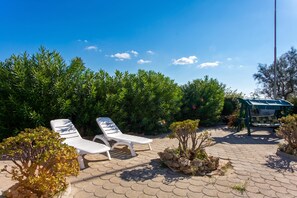 Un patio con dos sillones blancos, una mesita y una pérgola.