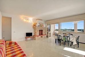 Un espacio habitable amplio con chimenea, un sofá, una mesa de comedor preparada para seis personas y ventanas grandes con vistas.