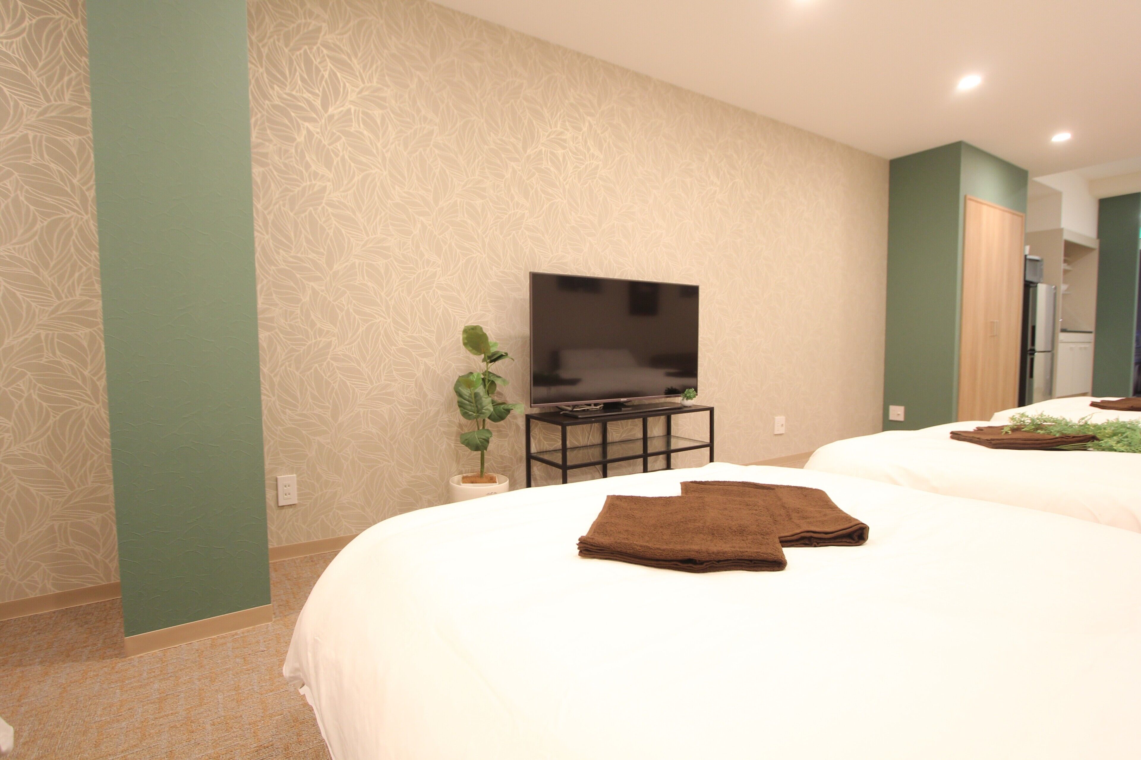 Une chambre d’hôtel avec un grand lit, un téléviseur à écran plat posé sur un meuble, une plante en pot et une serviette soigneusement pliée sur le lit.