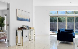 A spacious room with a large window, a blue sofa, a glass coffee table, and a painting on the wall. - Stunning Modern Oasis - Heated Pool & Spa · Mountain Views · 5min to Downtown! (Palm Springs)