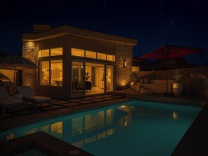 A modern house with a swimming pool, outdoor seating, and a well-lit interior. - Stunning Modern Oasis - Heated Pool & Spa · Mountain Views · 5min to Downtown! (Palm Springs)