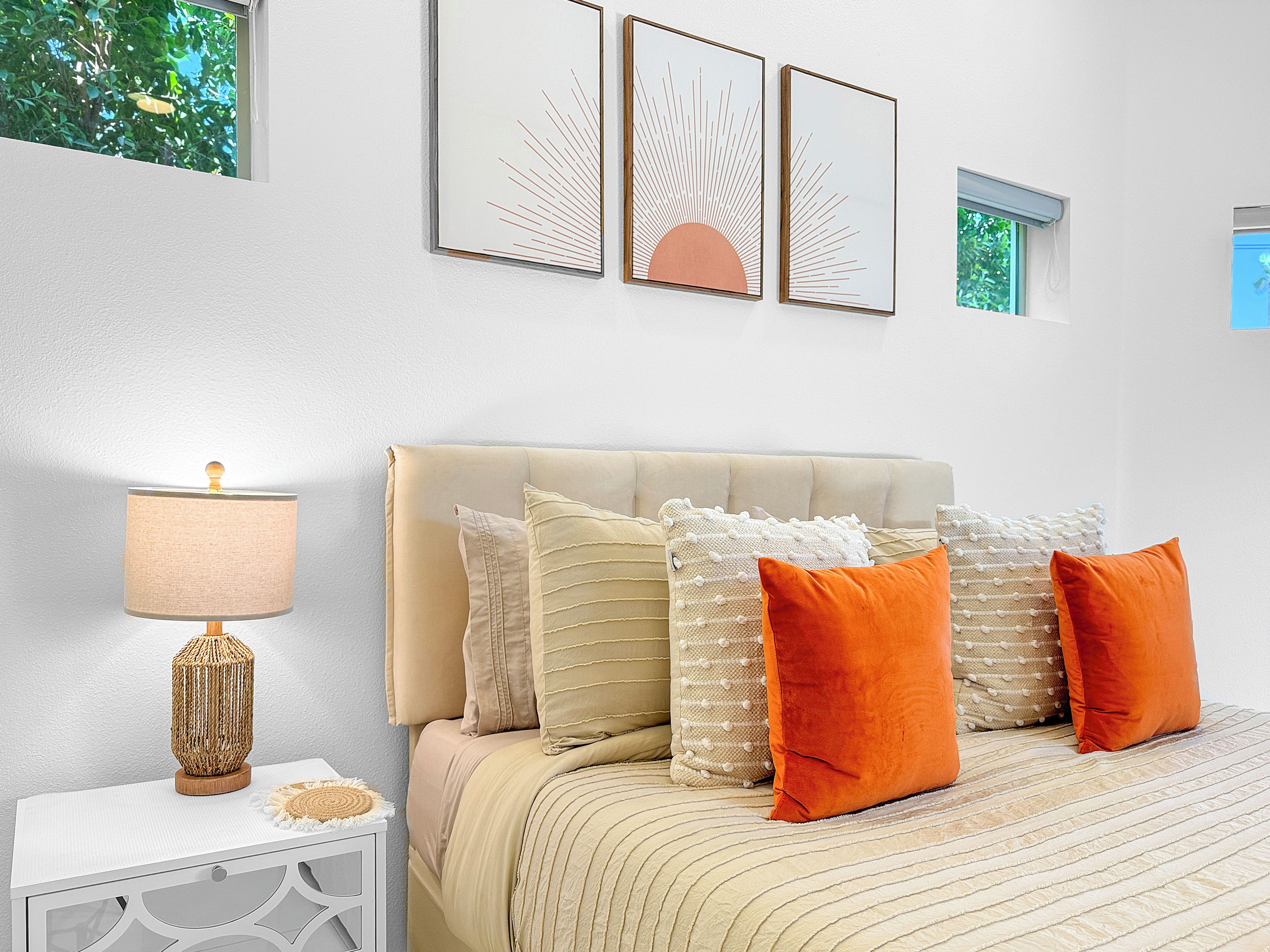 Ein Schlafzimmer mit einem Bett, Kissen, einem Nachttisch, einer Lampe und Wandbildern.