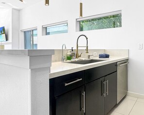 A modern kitchen with a white countertop, black cabinets, and a stainless steel dishwasher. - Stunning Modern Oasis - Heated Pool & Spa · Mountain Views · 5min to Downtown! (Palm Springs)
