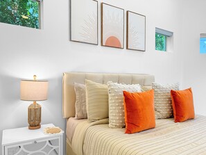 A bedroom with a bed, pillows, a bedside table, a lamp, and wall art. - Stunning Modern Oasis - Heated Pool & Spa · Mountain Views · 5min to Downtown! (Palm Springs)