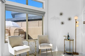 A modern interior with two chairs, a small table, decorative wall art, and a floor lamp. - Stunning Modern Oasis - Heated Pool & Spa · Mountain Views · 5min to Downtown! (Palm Springs)