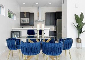 Una cocina moderna con una mesa de comedor de vidrio, sillas tapizadas en azul y electrodomésticos de acero inoxidable.