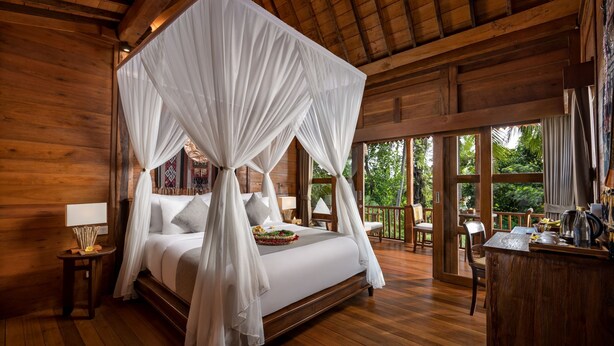 A wooden cabin with a four-poster bed, a small table with a lamp, and a balcony with a view of the outdoors. - Berlima Boutique Resort (Ubud)