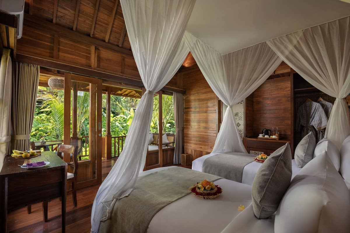 A room with two beds, a wooden ceiling, and a view of greenery outside.