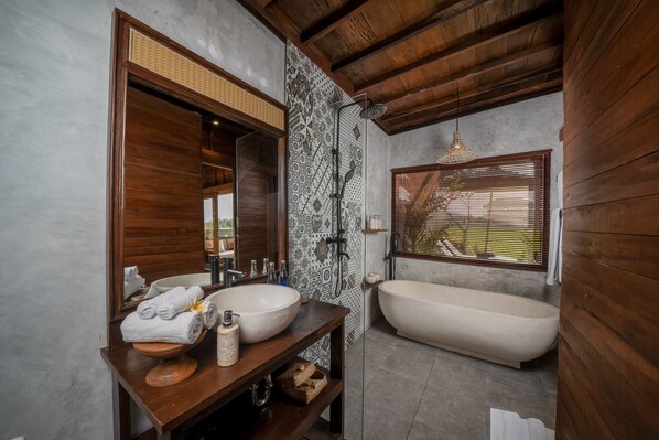 Un baño con tocador de madera, un lavamanos grande, una bañera y una ducha.