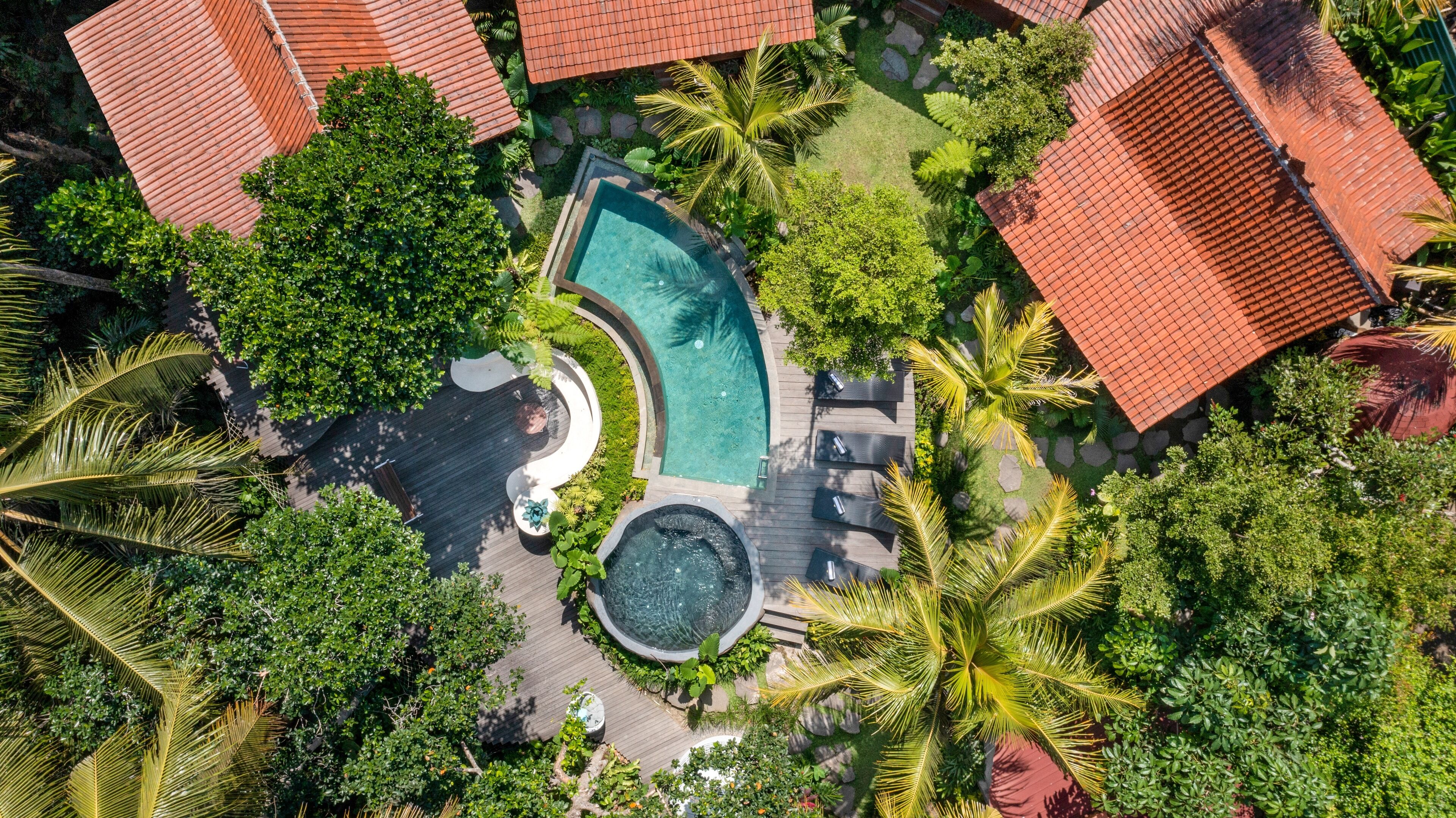 An aerial view of a resort with a swimming pool, lounge areas, and tropical landscaping.