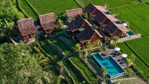 A resort with multiple wooden villas, a swimming pool, and lush green fields. - Berlima Boutique Resort (Ubud)