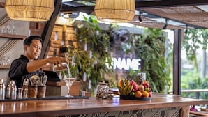 Eine Bar mit Barkeeper, Obstschale und einem 'NAME' Schild im Hintergrund.