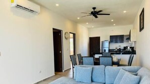 Una sala de estar moderna con un sofá seccional gris, un comedor con sillas, una cocina con gabinetes oscuros y un ventilador de techo.