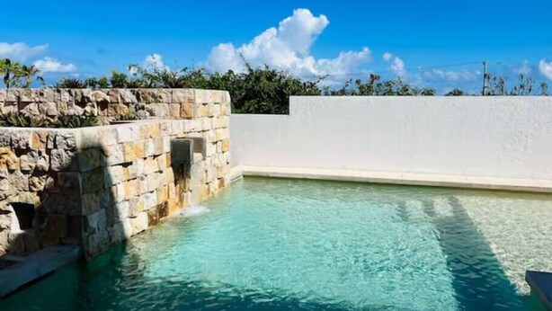 Una piscina azul cristalina con un muro de piedra y un muro blanco al fondo.