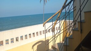 Un escalier menant à un balcon d’où l’on peut admirer une plage, un palmier et la mer.