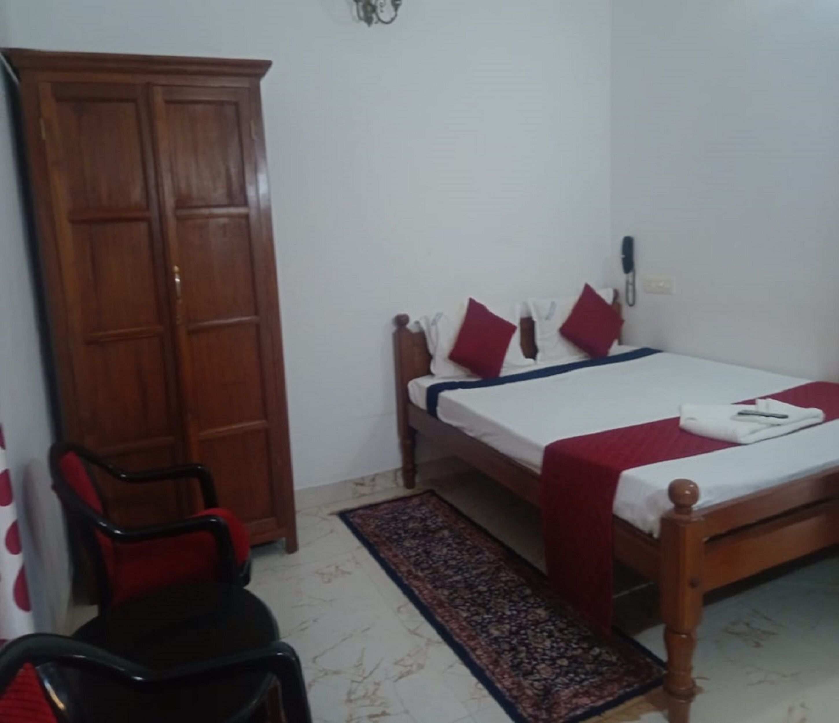 A bedroom with a wooden bed, red and white bedding, a wooden wardrobe, and a red chair.