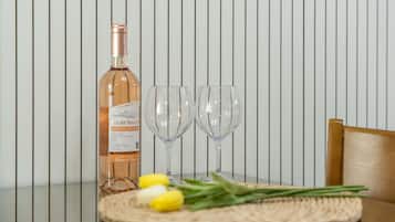 A bottle of wine, two wine glasses, and a woven placemat with yellow flowers on a table against a striped wall.