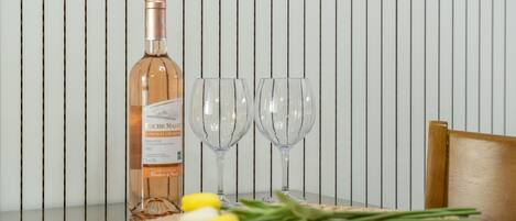 Een fles wijn, twee wijnglazen en een geweven onderzetter met gele bloemen op een tafel tegen een gestreepte muur.