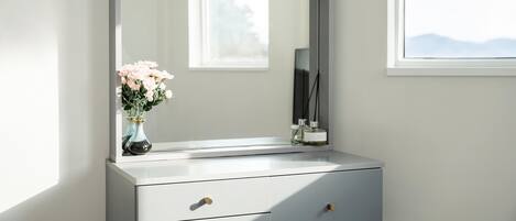 A bathroom vanity with a large mirror, two drawers, and a vase with flowers.