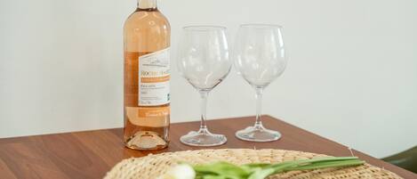 A bottle of wine, two empty wine glasses, and a woven placemat with some flowers on a wooden table.
