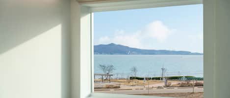 Ein Fenster mit Blick auf ein Gewässer, ein ferner Berg und ein Park mit Bänken und Bäumen.