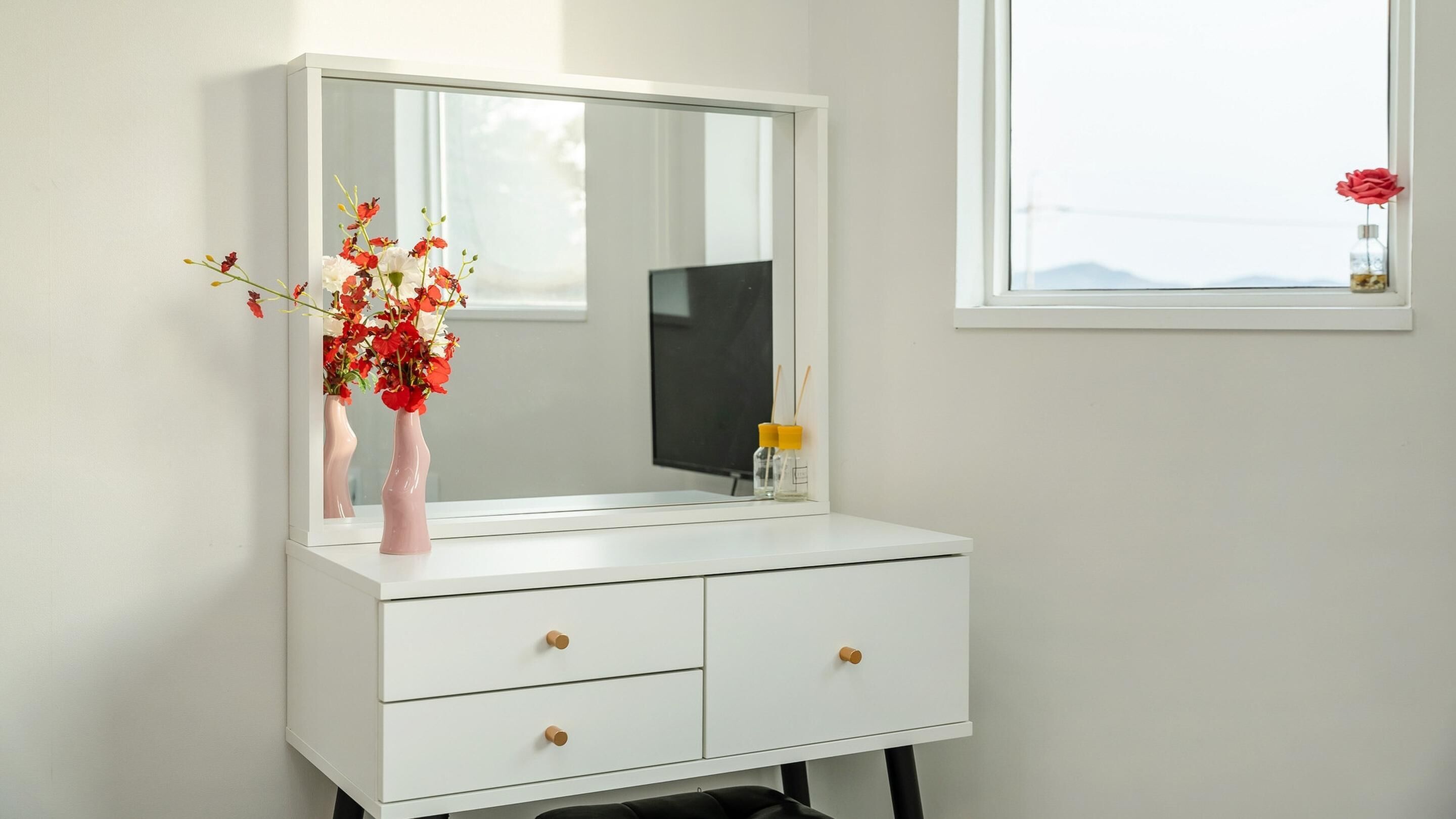 A white vanity with a large mirror, two drawers, and a small window with a red rose.