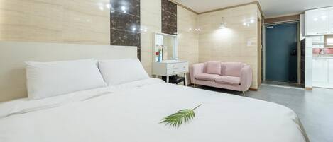 A hotel room with a large bed, a small desk, a pink chair, and a bathroom visible through an open door.
