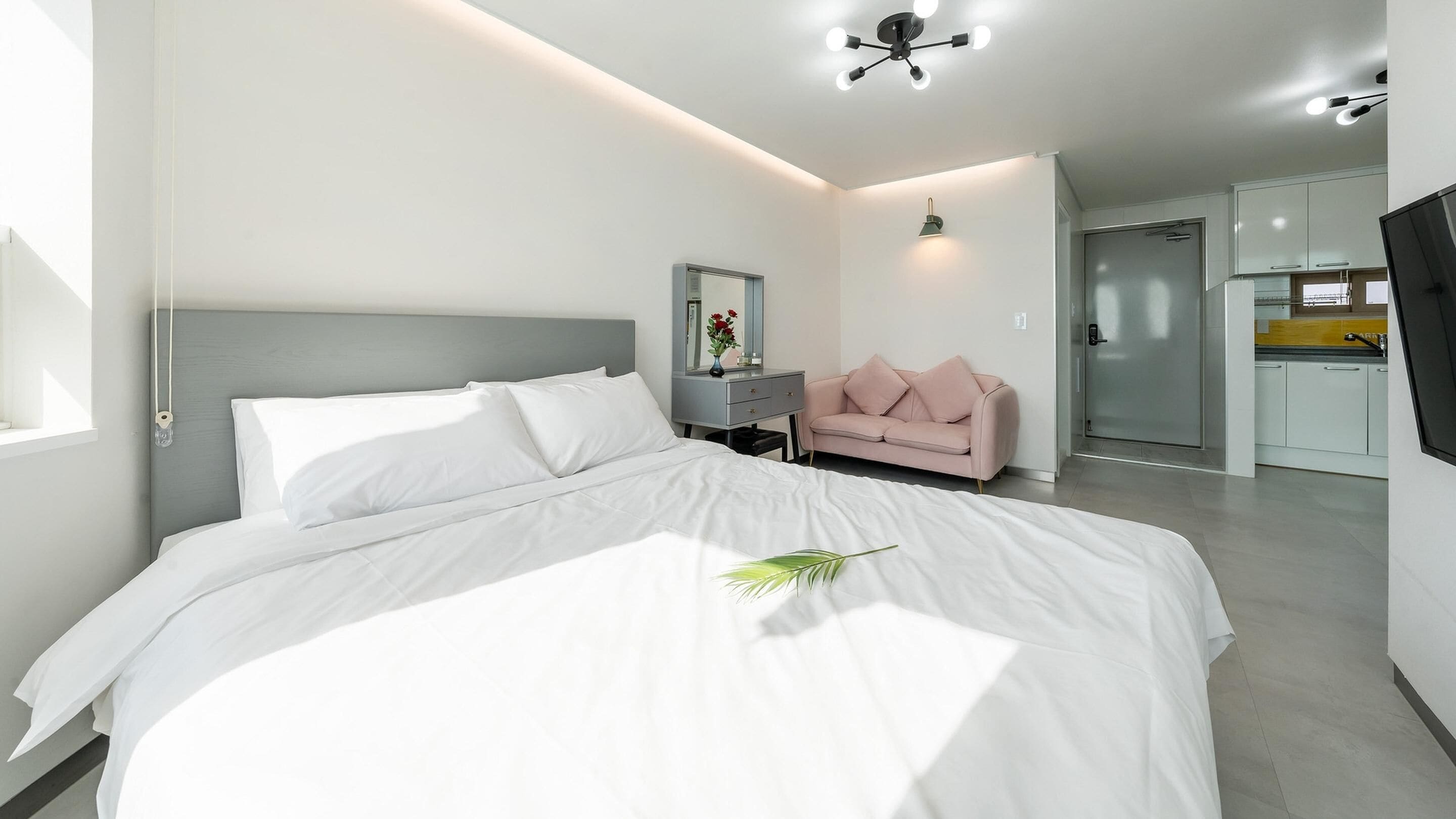 A modern bedroom with a large bed, a bedside table, a pink sofa, and a TV.