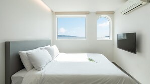 Een slaapkamer met een bed, twee ramen, een flatscreen-tv en een airconditioning.