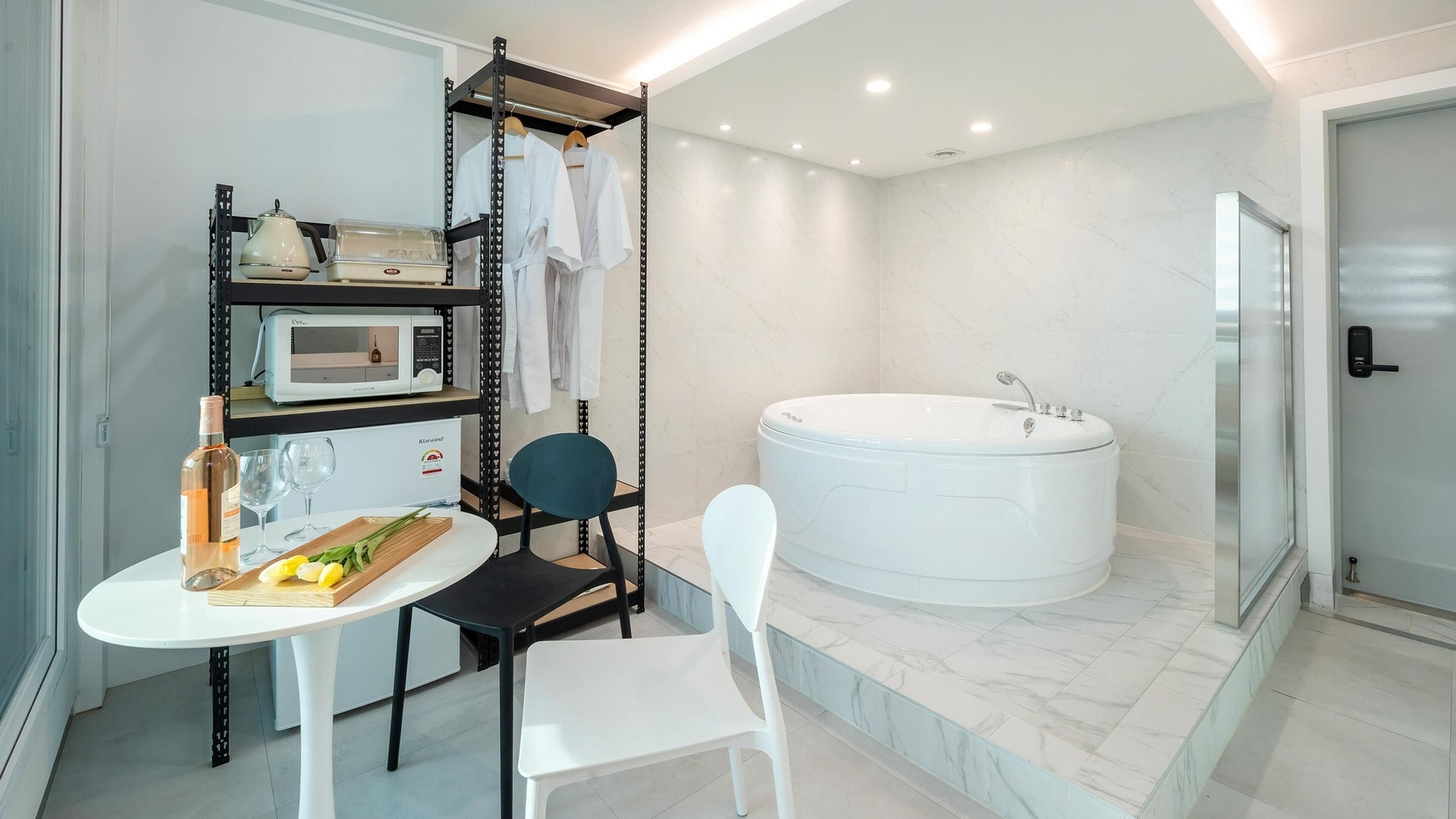 Un bagno moderno con una vasca da bagno ampia, un tavolino con una bottiglia e dei bicchieri, e una sedia.
