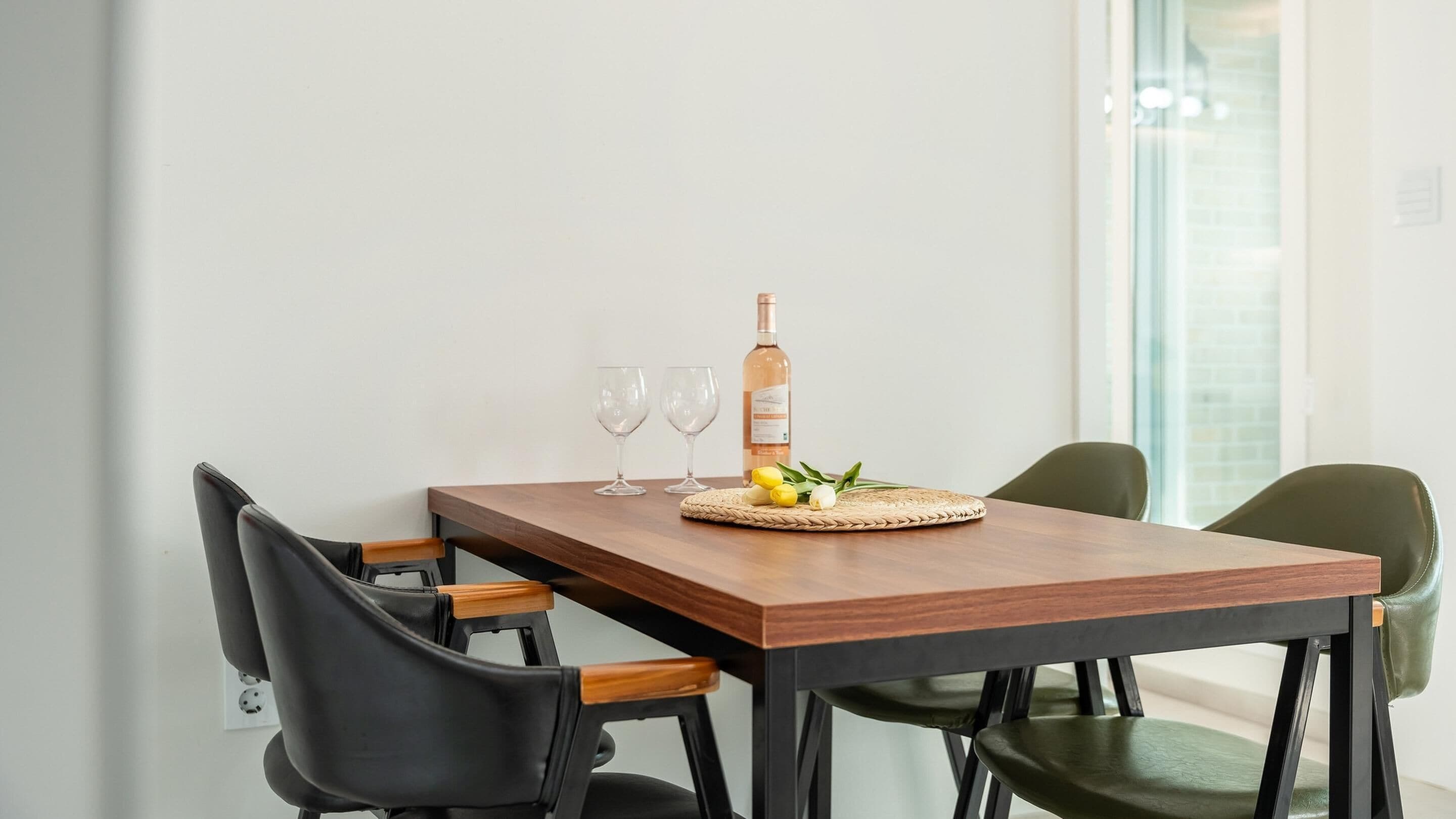 A wooden dining table with two chairs, a bottle, and a woven placemat with lemons and garlic.