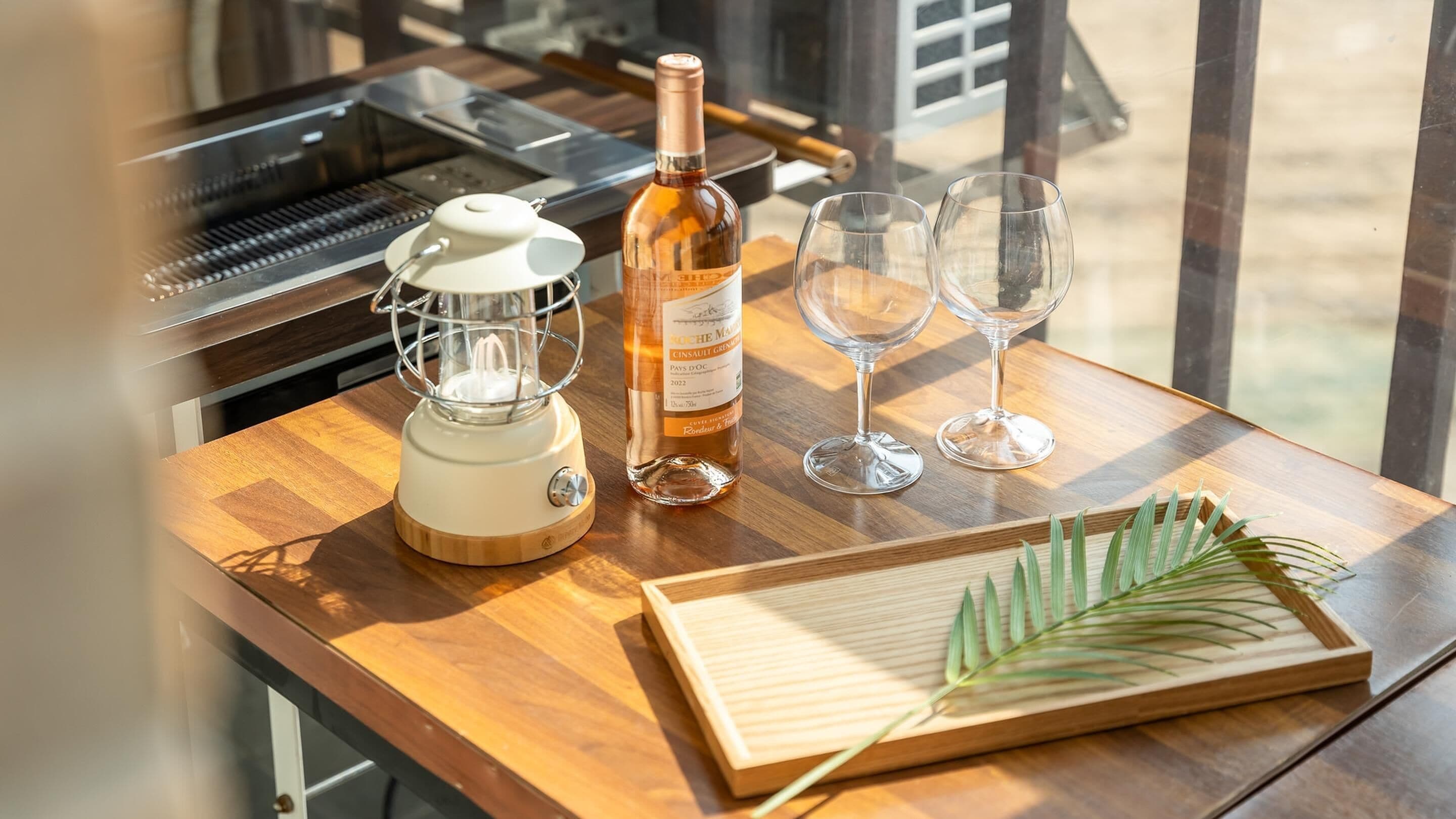 Una mesa de madera con un exprimidor, una botella de vino, dos copas y una tabla de madera con una planta verde.