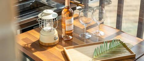 Una mesa de madera con un exprimidor, una botella de vino, dos copas y una tabla de madera con una planta verde.