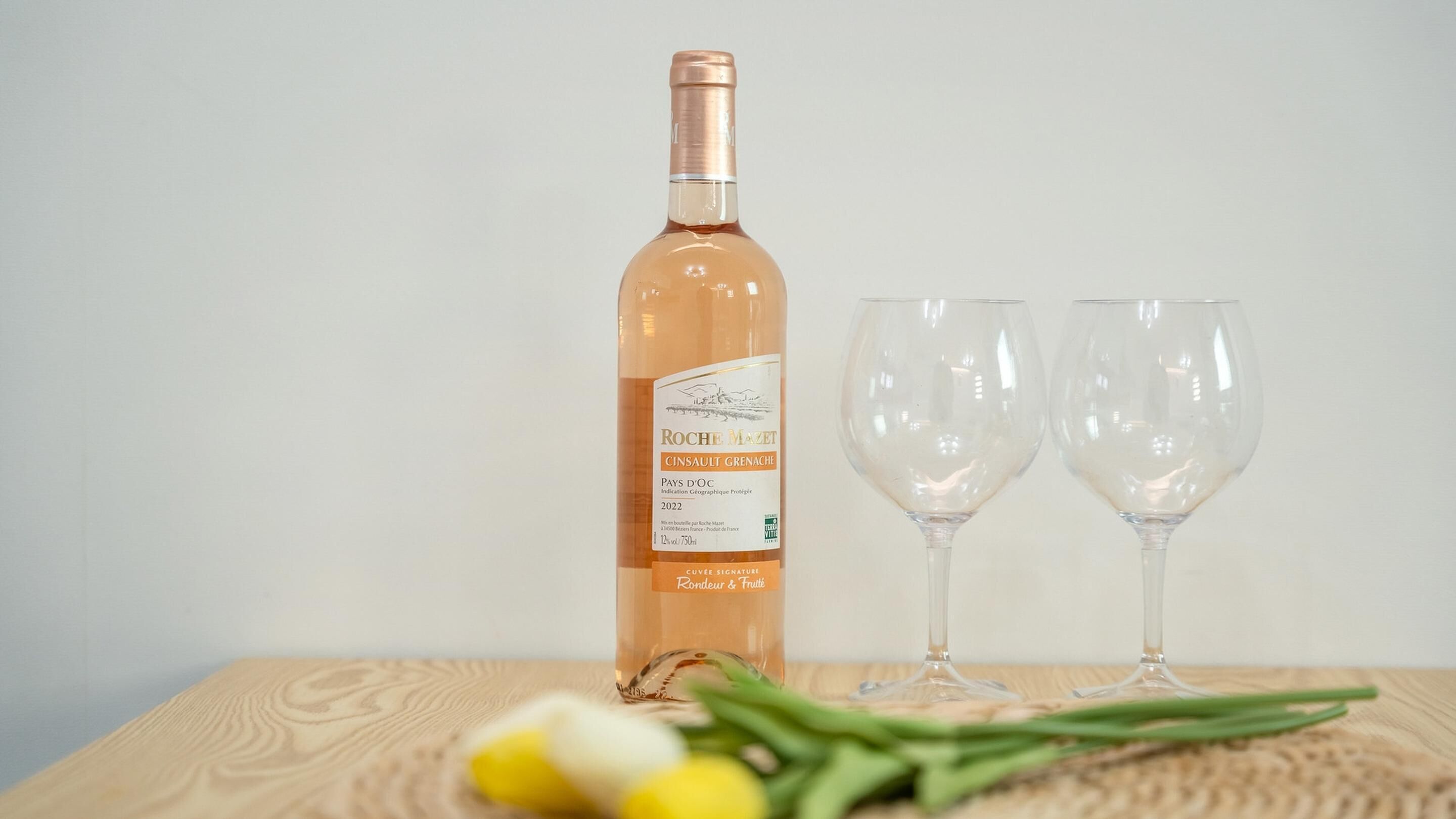 A bottle of wine and two empty wine glasses on a wooden table.